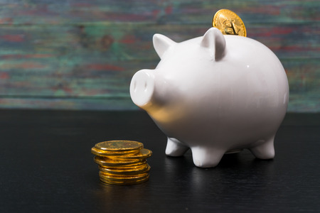White piggy bank with one gold bitcoin coin new virtual money on a colored wooden backgroundの写真素材