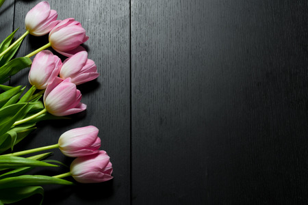 Border from bright pink tulips flowers on black wooden background. Selective focus. Place for text. Flat lay.の写真素材