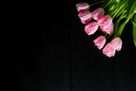Border from bright pink tulips flowers on black wooden background. Selective focus. Place for text. Flat lay.の写真素材