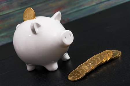 White piggy bank with one gold bitcoin coin new virtual money on a colored wooden backgroundの写真素材