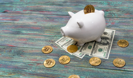 White piggy bank with one gold bitcoin coin new virtual money on a colored wooden backgroundの写真素材