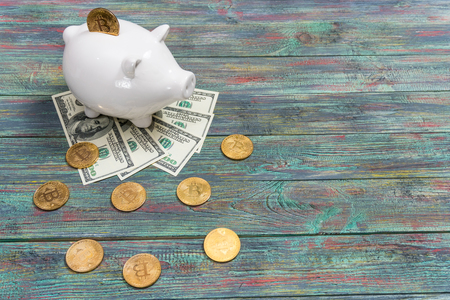 White piggy bank with one gold bitcoin coin new virtual money on a colored wooden backgroundの写真素材