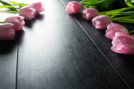 Border from bright pink tulips flowers on black wooden background. Selective focus. Place for text. Flat lay. With an artificial Sun Reflexの写真素材