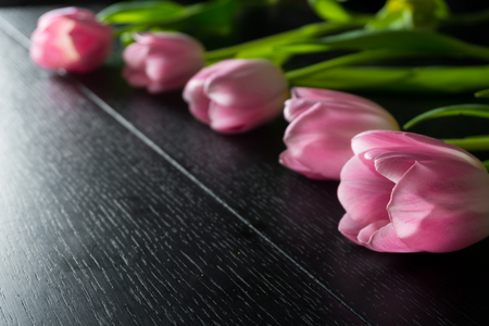 Border from bright pink tulips flowers on black wooden background. Selective focus. Place for text. Flat lay. With an artificial Sun Reflexの写真素材