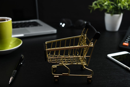The concept of online shopping. Gold cart, cash and gadgets on a black table.の写真素材