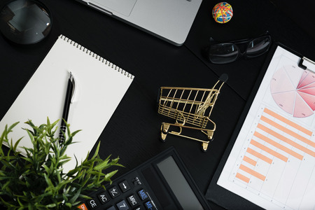 The concept of online shopping. Gold cart, cash and gadgets on a black table.の写真素材
