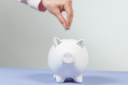 Hand putting coin into piggy bank closeup. Selective focus. Piggy Bank, Savings, Currency.の写真素材