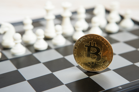 Golden bitcoin coin symbolizes elements of virtual economy or crypto currency with chess boardの写真素材
