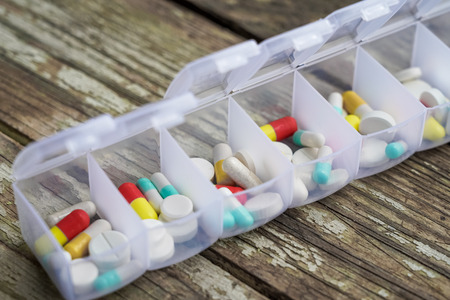 Variety of pills in white plastic pill organizer on weathered wood, free space for textの写真素材