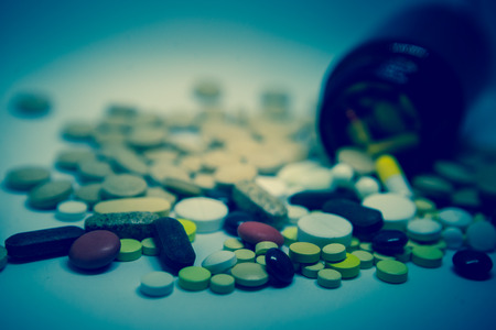 Pile of multicolored tablets and medicine lying on a white surface. Close up.   Selective focus/toned photoの写真素材