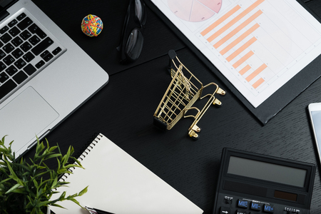 The concept of online shopping. Gold cart, cash and gadgets on a black table.の写真素材