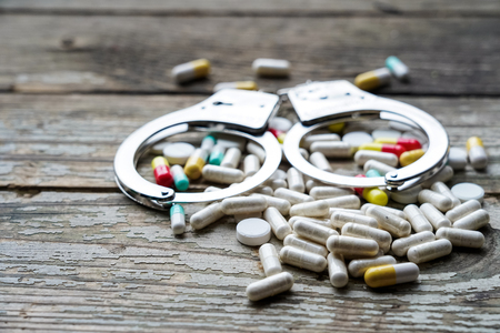 Handcuffs and pills and drugs on wooden table. Selective focusの写真素材