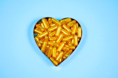 Heart shaped of gold pills on blue paper background. Copy space for textの写真素材