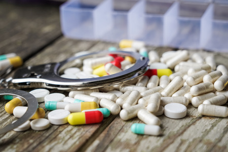 Handcuffs and pills and drugs on wooden table. Selective focusの写真素材