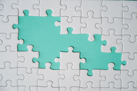 Missing jigsaw puzzle pieces. Business concept. Fragment of a folded white jigsaw puzzle and a pile of uncombed puzzle elements against the background of a colored surface.の写真素材