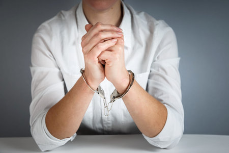 Close-up. Arrested man handcuffed hands at the back isolated on gray background. Prisoner or arrested close-up of hands in handcuffs.の写真素材
