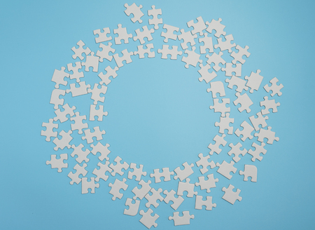 Missing jigsaw puzzle pieces. Business concept. Fragment of a folded white jigsaw puzzle and a pile of uncombed puzzle elements against the background of a blue surface.の写真素材