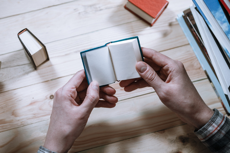 A man reading a miniature book among the big books in the library at the wooden table.の写真素材