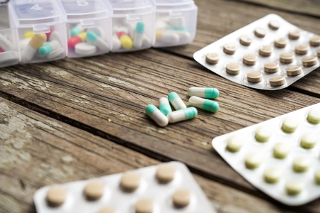 Variety of pills in white plastic pill organizer on weathered wood, free space for textの写真素材