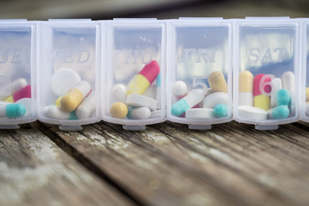 Variety of pills in white plastic pill organizer on weathered wood, free space for text