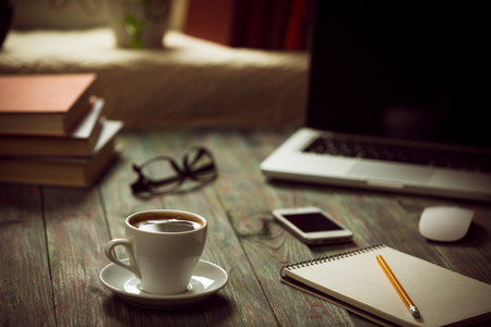 A cup of coffee in the workplace on a wooden table. A cup of coffee in the workplace on a wooden table. The concept of working outside the officeの写真素材