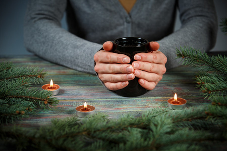 Woman holds a cup of hot tea among the fir branches and candle. Cozy morning at home. With copy spaceの写真素材
