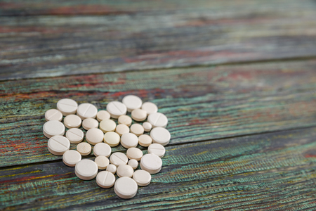 White pills in the shape of a heart on a wooden background with copy space. Global healthcare concept. Pharmaceutical industry. Pharmacy.の写真素材