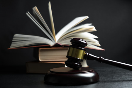 Judge gavel beside pile of books on black wooden backgroundの写真素材