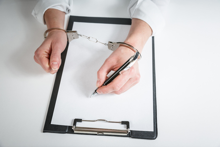 Female hands in handcuffs fill out police report recognition. Arrest, bail, criminal, prison.の写真素材