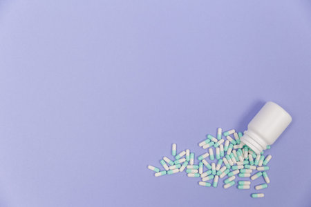 Blue and white capsules pill spilled out from white plastic bottle container. Global healthcare...