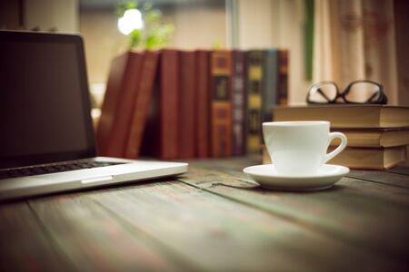 A cup of coffee in the workplace on a wooden table. A cup of coffee in the workplace on a wooden table. The concept of working outside the officeの写真素材