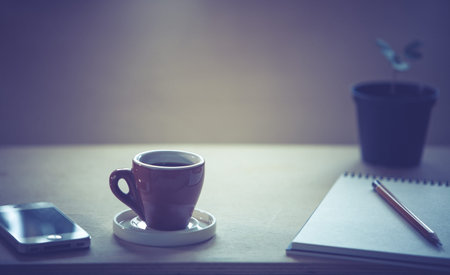 Cup of fresh coffee  with notebook and pencil on wooden table. Selective focus. 