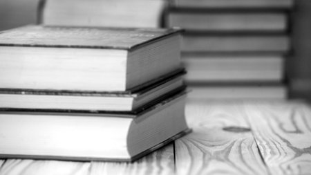 Textbooks and books on a wooden table. Book stack in the library room and blurred bookshelf for...