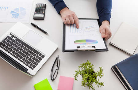 Businessman holding a pen is working with graph documents and sunset light background. Stock market chart and finger pointing on tablet in office.の写真素材