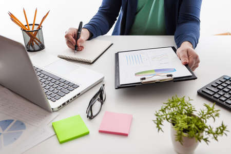 Businessman holding a pen is working with graph documents and sunset light background. Stock market chart and finger pointing on tablet in office.の写真素材