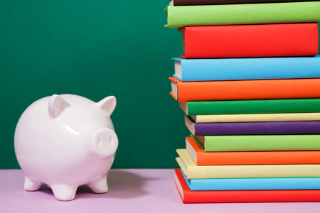 Composition with piggy bank and hardback books, diary, fanned pages on wooden deck table and colored...