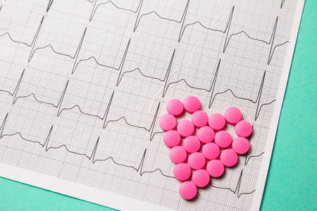 A pile of red pills in a shape of heart on cardiogram. Medical concept.の写真素材