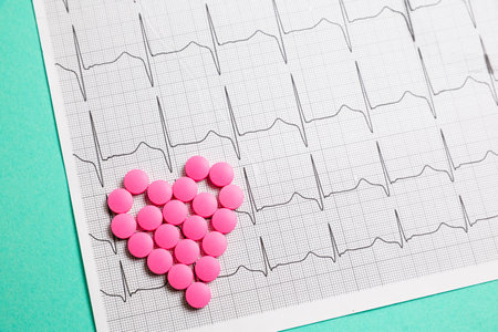 A pile of red pills in a shape of heart on cardiogram. Medical concept.の写真素材