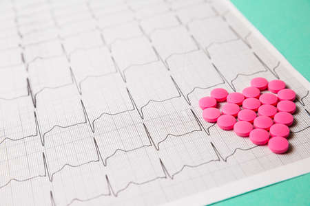 A pile of red pills in a shape of heart on cardiogram. Medical concept.の写真素材