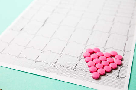 A pile of red pills in a shape of heart on cardiogram. Medical concept.の写真素材