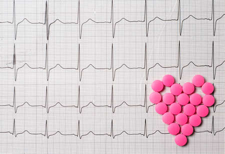 A pile of red pills in a shape of heart on cardiogram. Medical concept.の写真素材