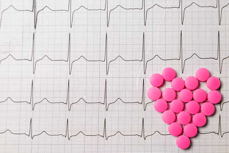 A pile of red pills in a shape of heart on cardiogram. Medical concept.の写真素材