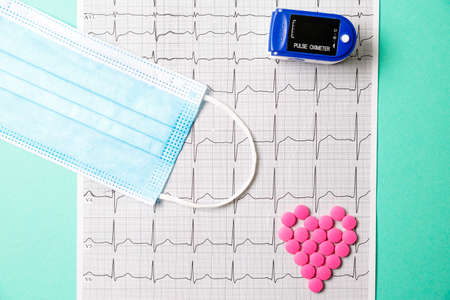 A pile of red pills in a shape of heart on cardiogram whis pulse oximeter. Medical concept.の写真素材