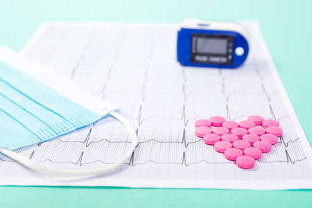 A pile of red pills in a shape of heart on cardiogram whis pulse oximeter. Medical concept.の写真素材