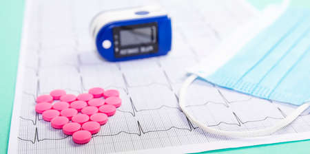 A pile of red pills in a shape of heart on cardiogram whis pulse oximeter. Medical concept.の写真素材