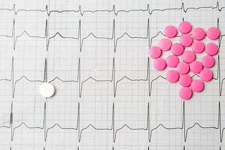A pile of red pills in a shape of heart on cardiogram. Medical concept.の写真素材