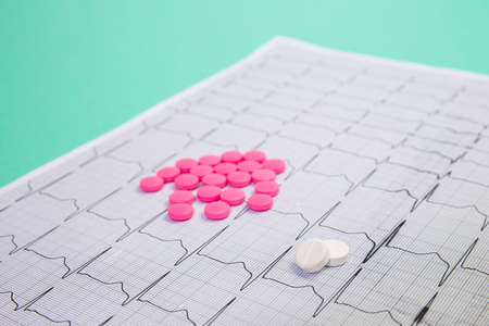 A pile of red pills in a shape of heart on cardiogram. Medical concept.の写真素材