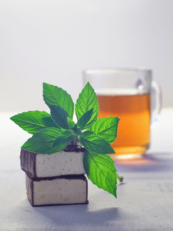 Chocolate glazed soufflé candies with cup of tea and mint leaf upon wooden tableの写真素材