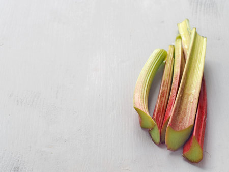 Freshly cut rhubarb upon wooden table. Red rhubarb stems with water drops. Culinary background. Copy...