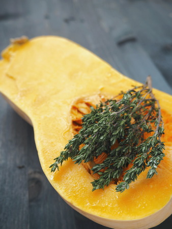 Close up of a ripe pumpkin halved on a wooden table with thyme sprigs. Selective focus on the center. Copy space for your text.の写真素材